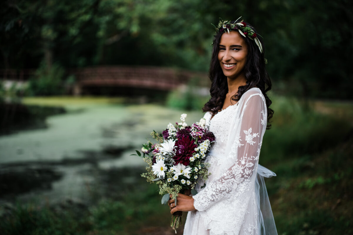 Bride poses with bouquet by a lake and smiles at Blue Mountain Reservation before a Hudson Valley Wedding at The Dramatic Hall in Peekskill New York