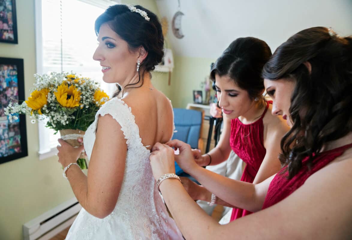 Bridesmaids helps bride into her wedding dress before her Hudson Valley Wedding At West Hills Country Club In Middletown, New York