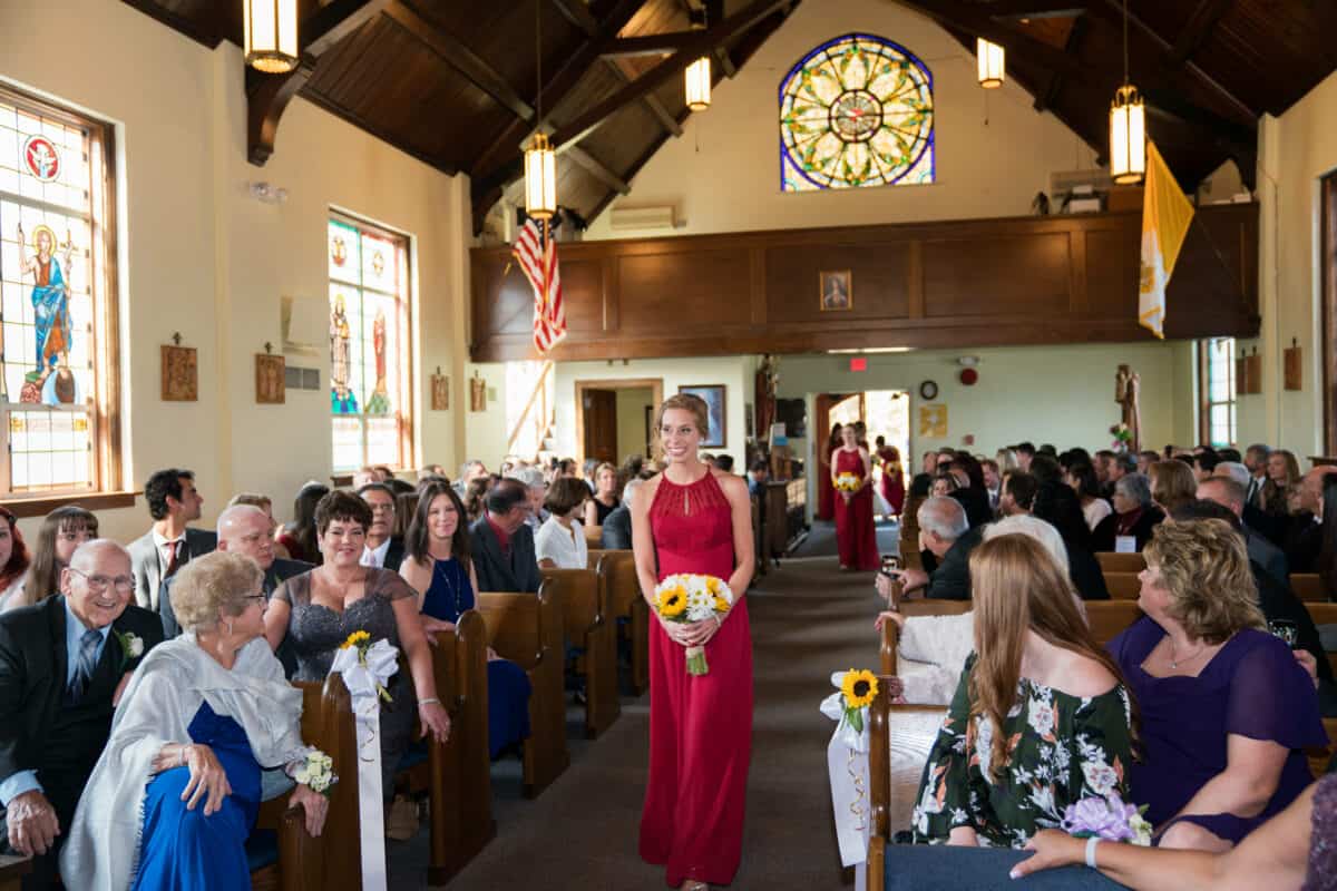 Bridesmaid walks down a church aisle at a Hudson Valley Wedding At West Hills Country Club In Middletown, New York