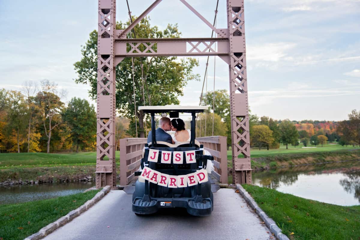 Bride and Groom kiss in golf cart on Bridge  at a Hudson Valley Wedding At West Hills Country Club In Middletown, New York