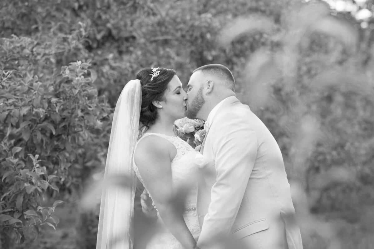 Bride and groom kiss in a field at Hudson Valley Wedding at Nostranos Vineyard