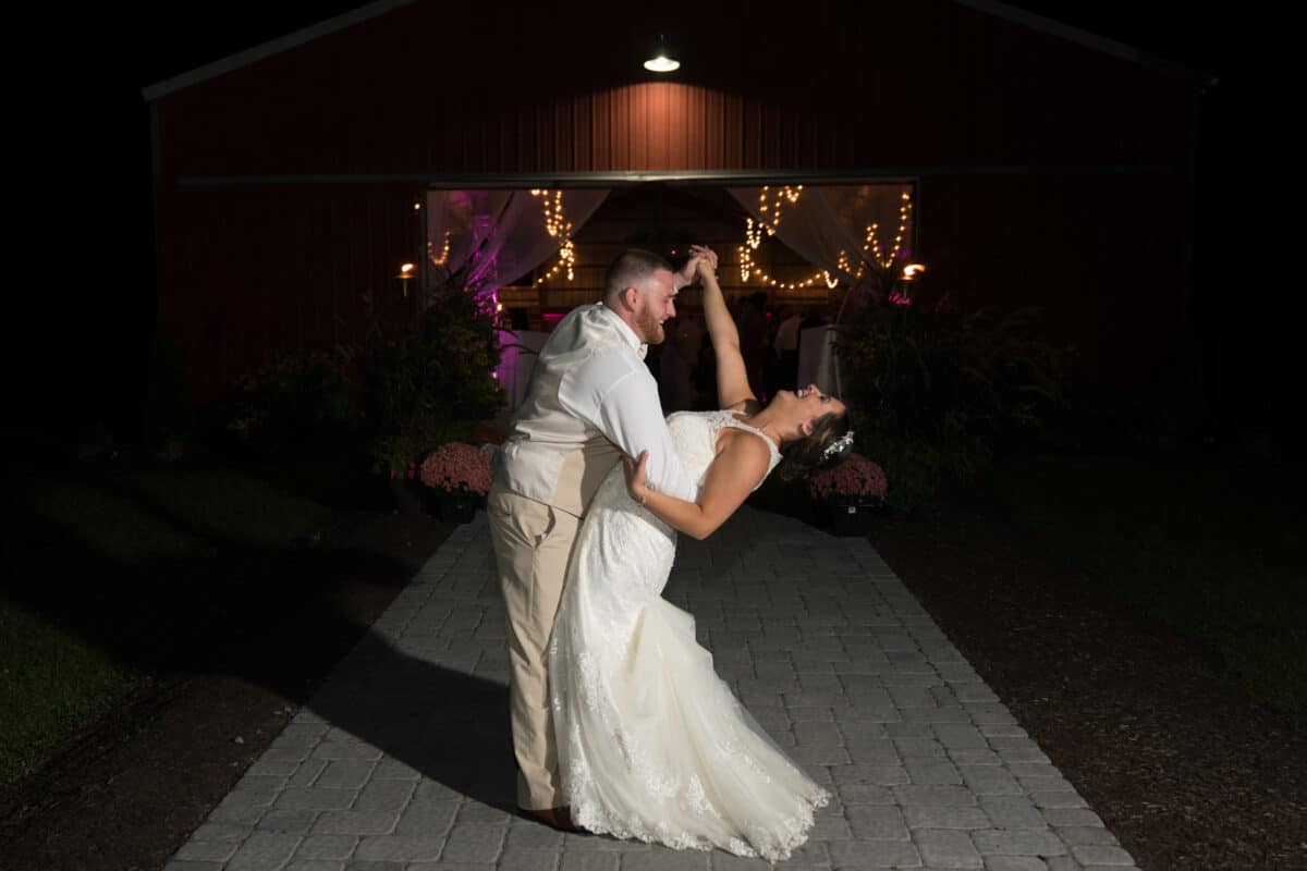 Groom dips bride infant of barn at Hudson Valley Wedding at Nostranos Vineyard