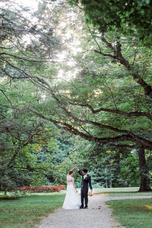 Groom twirls bride under trees after Hudson Valley Ceremony At Locust Grove in Poughkeepsie