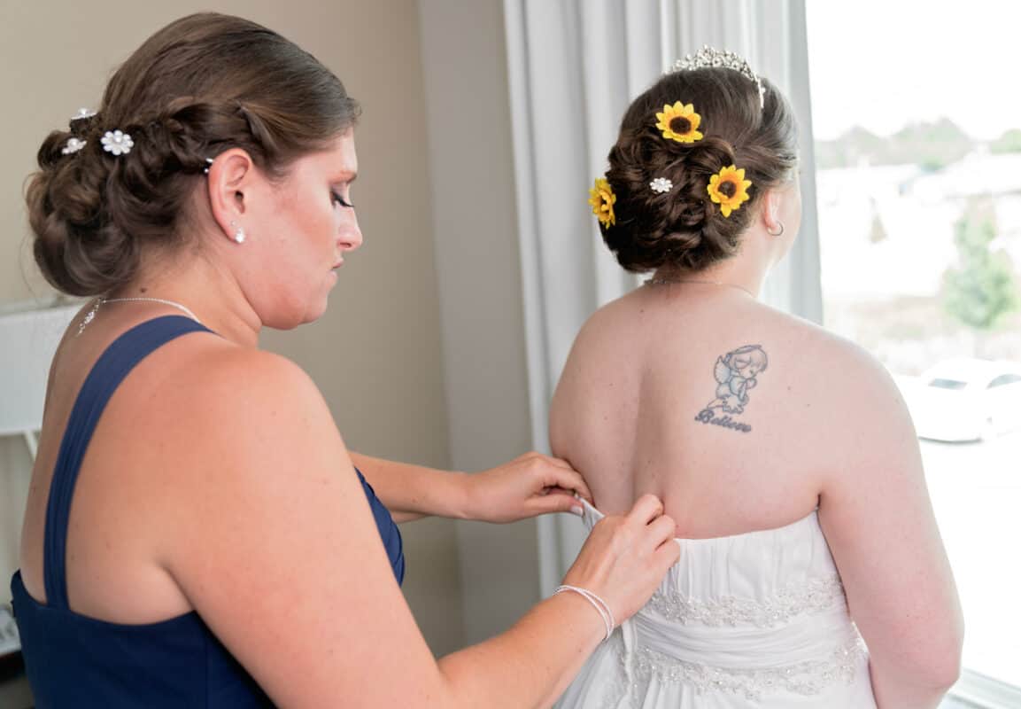 Bridesmaid zipping brides dress while getting ready for her Hudson Valley same sex wedding At Lippincott Manor in Walkill New York