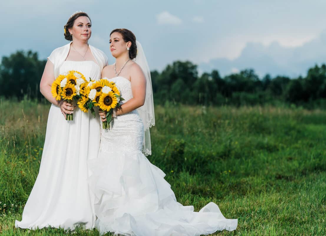 Bride and bride stand in front of a field at Hudson Valley same sex wedding At Lippincott Manor in Walkill New York