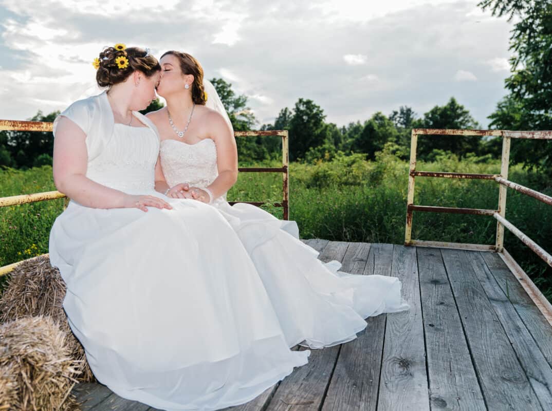 Bride and bride kissing rustic cart at Hudson Valley same sex wedding At Lippincott Manor in Walkill New York