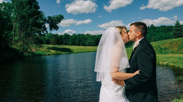 Bride and grooms kiss by lake at their Albany Wedding at Sweet Basile Restaurant