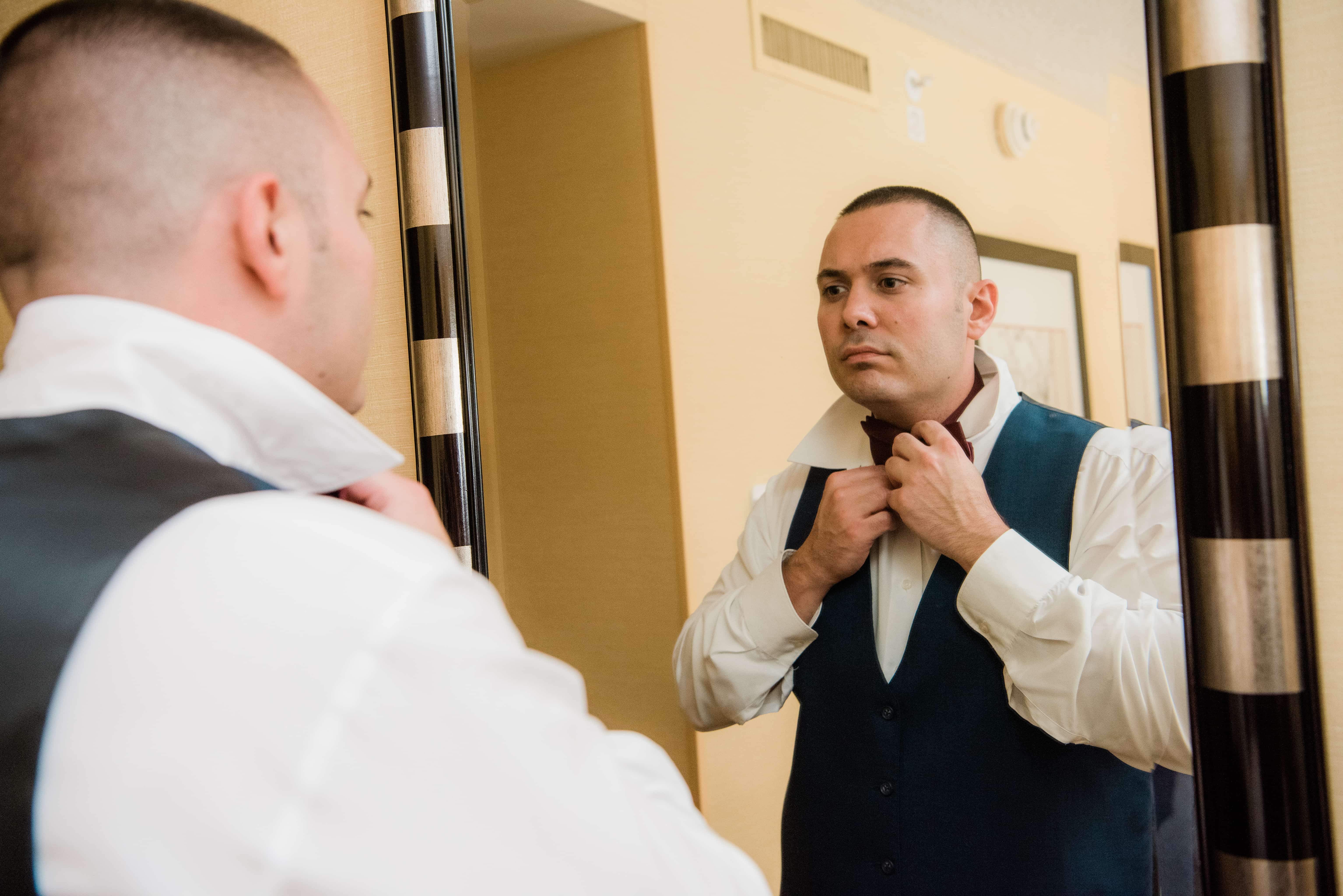 Groom fixes bowtie while getting ready at a Hudson Valley Wedding at Brotherhood Winery