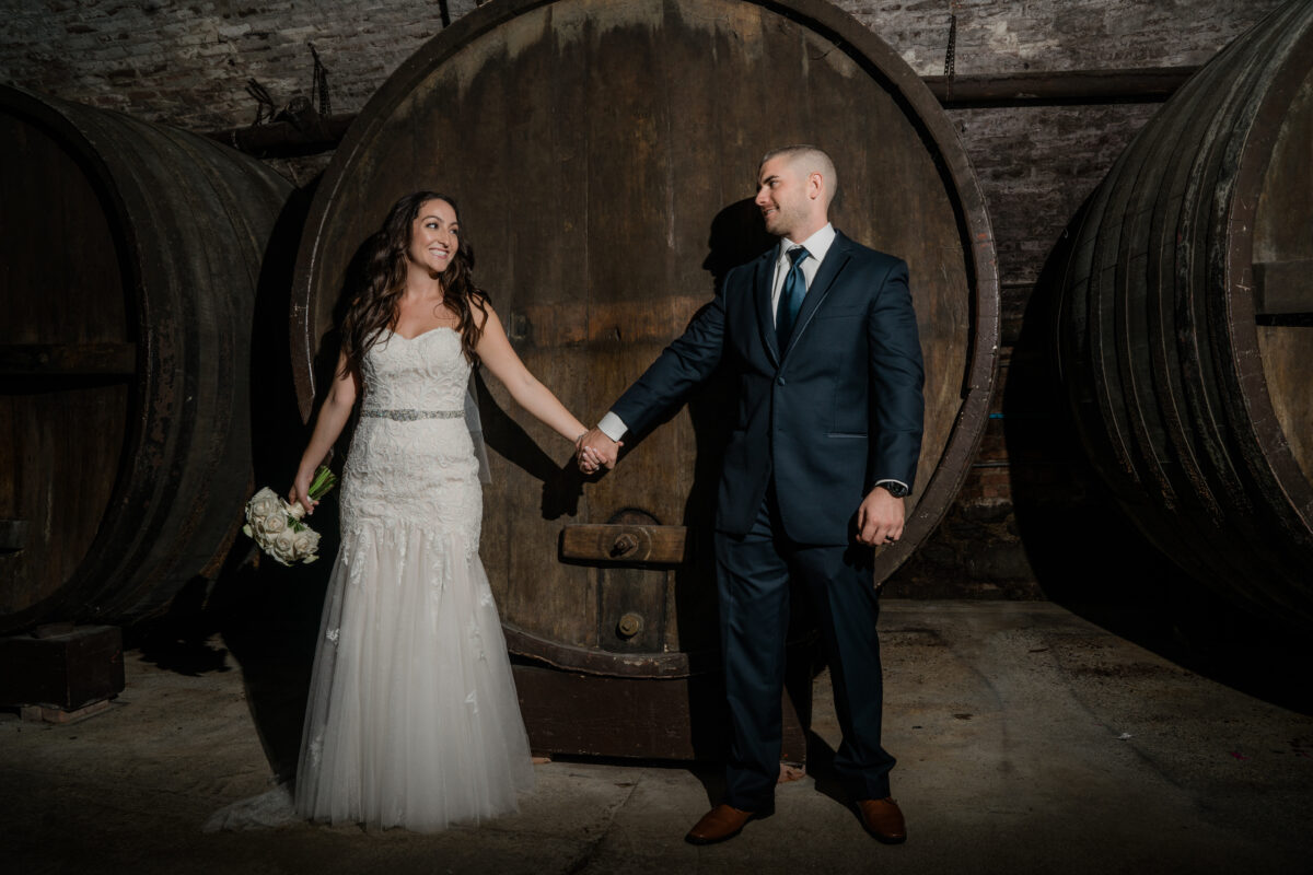 Bride and Groom pose by wine barrels at a Hudson Valley Wedding at the Brotherhood Winery