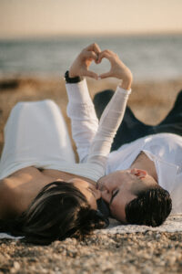 Bride and Groom Lay on a towel and make a heart with hands for an Engagement Photo at Greenwich Point Park in Greenwich Connecticut