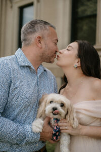 Bride and Groom Kiss while holding dog at a Hudson Valley Engagement Shoot at Vanderbilt Estate in Hyde Park New York.