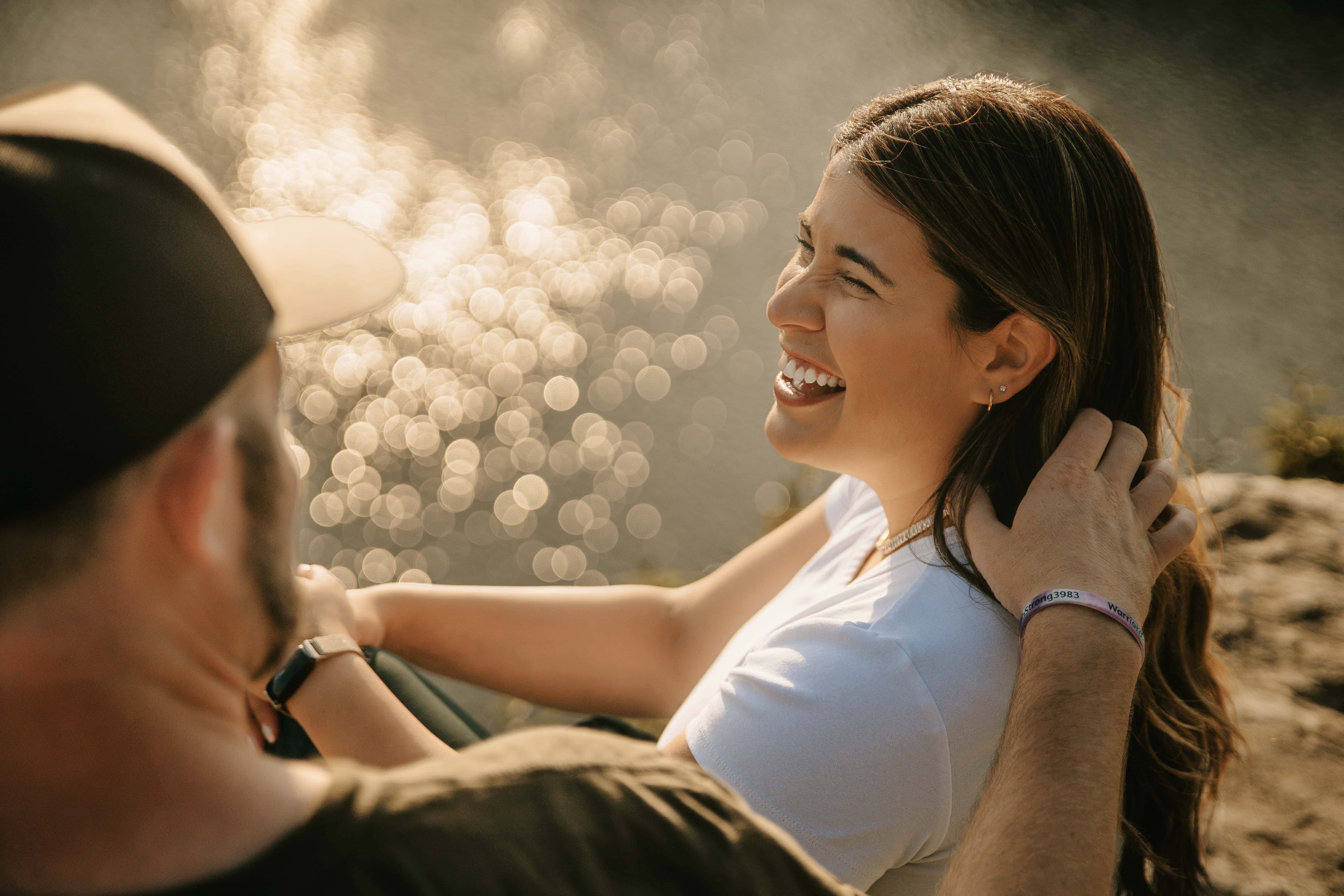 Bride smiles and laughs with groom along a cliff by a lake for a Hudson Valley Engagement Photo in Minnewaska State Park