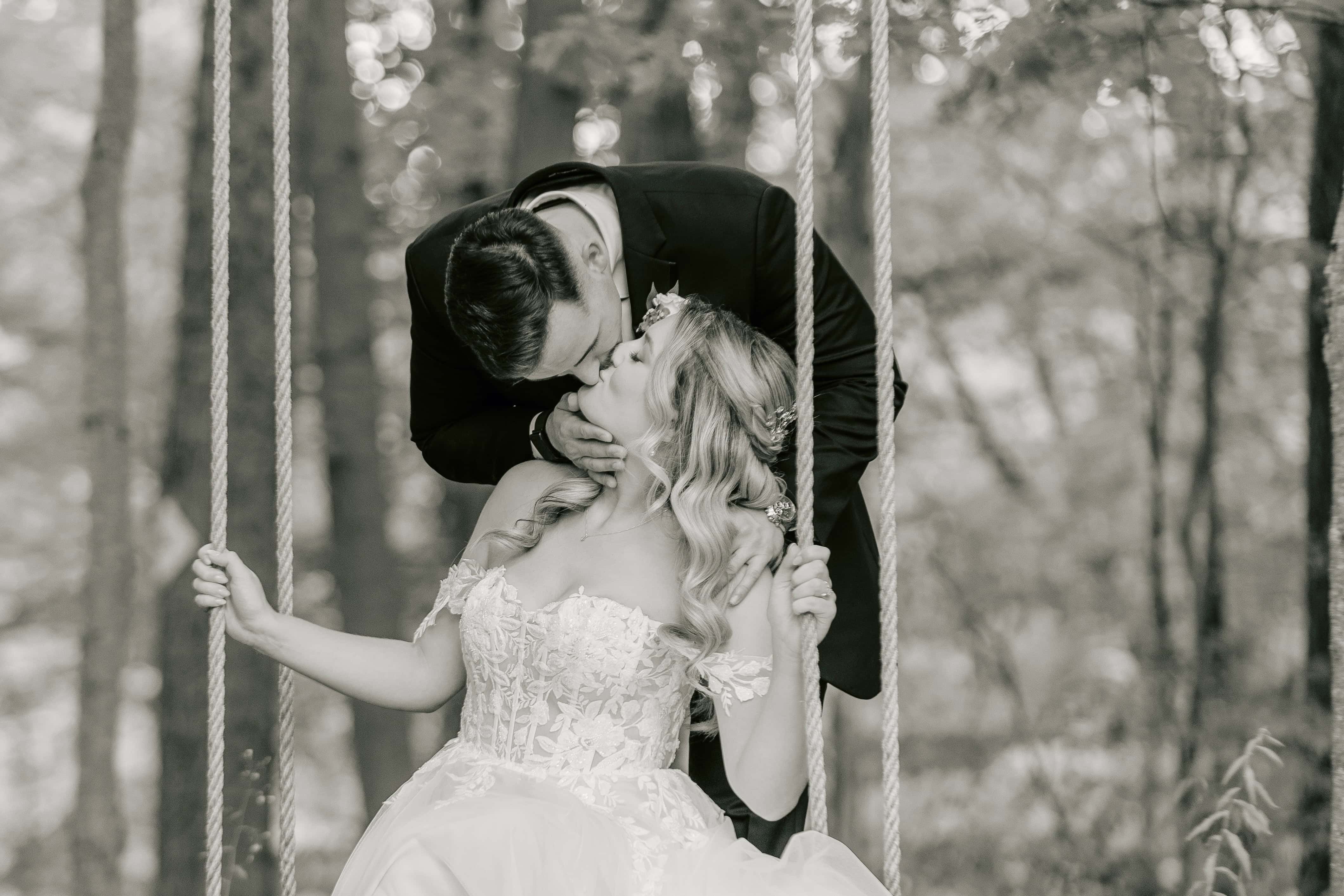 Black and White photo of Groom Kissing Bride on Swing for a New Jersey Wedding Photo at Rock island Lake Club