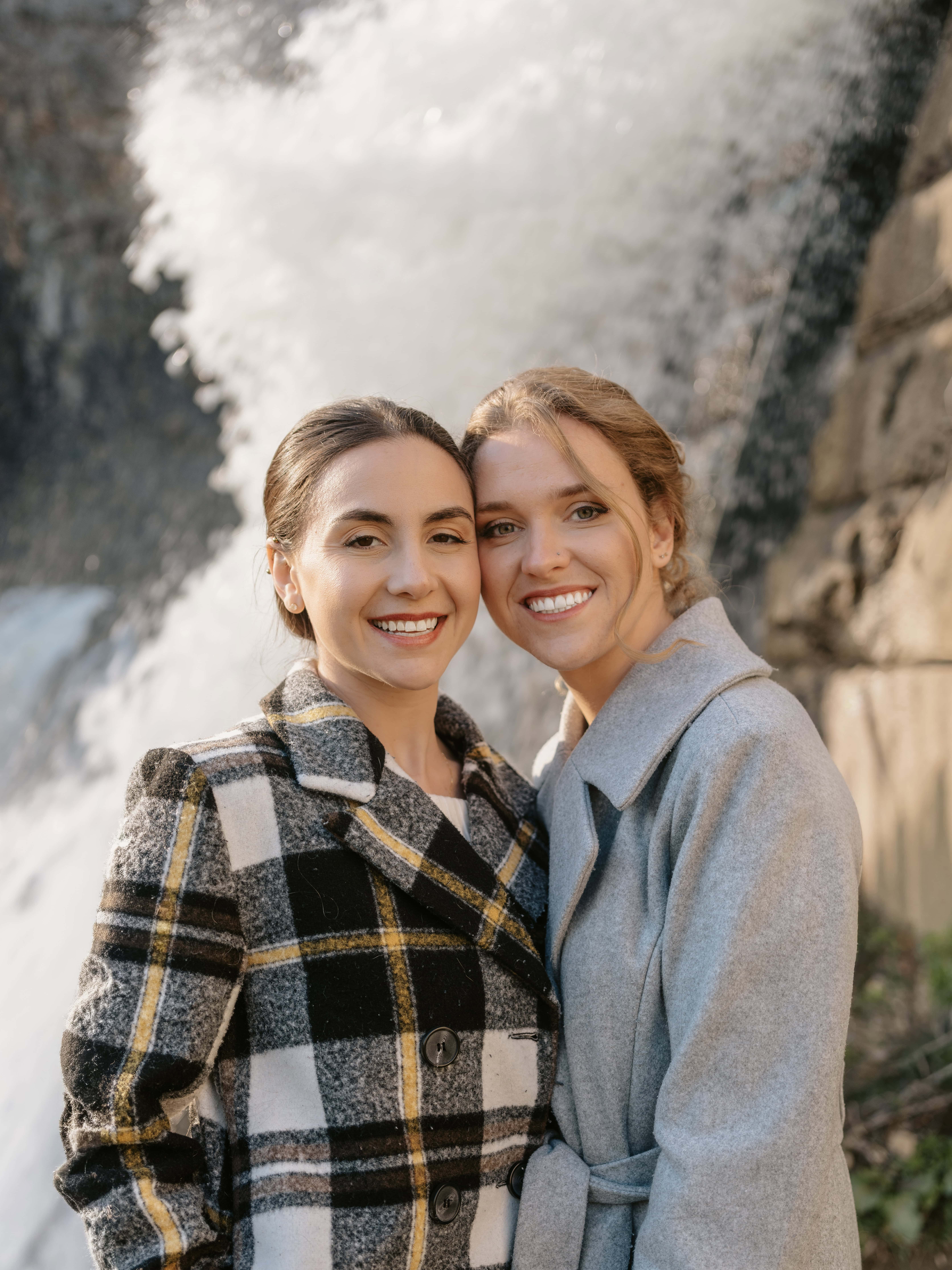 Brides smile by waterfall at a Croton Gorge Park Engagement Shoot in the Hudson Valley