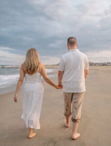 Bride and Groom hold hands and walk along the beach at Sunset for a Asbury Park Engagement Photo
