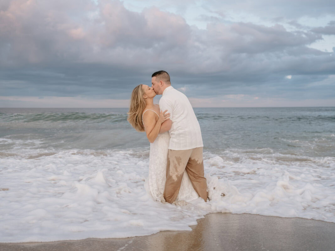 Groom dips bride and kiss on beach in Waves and Surf at Sunset for a Asbury Park Engagement Photo