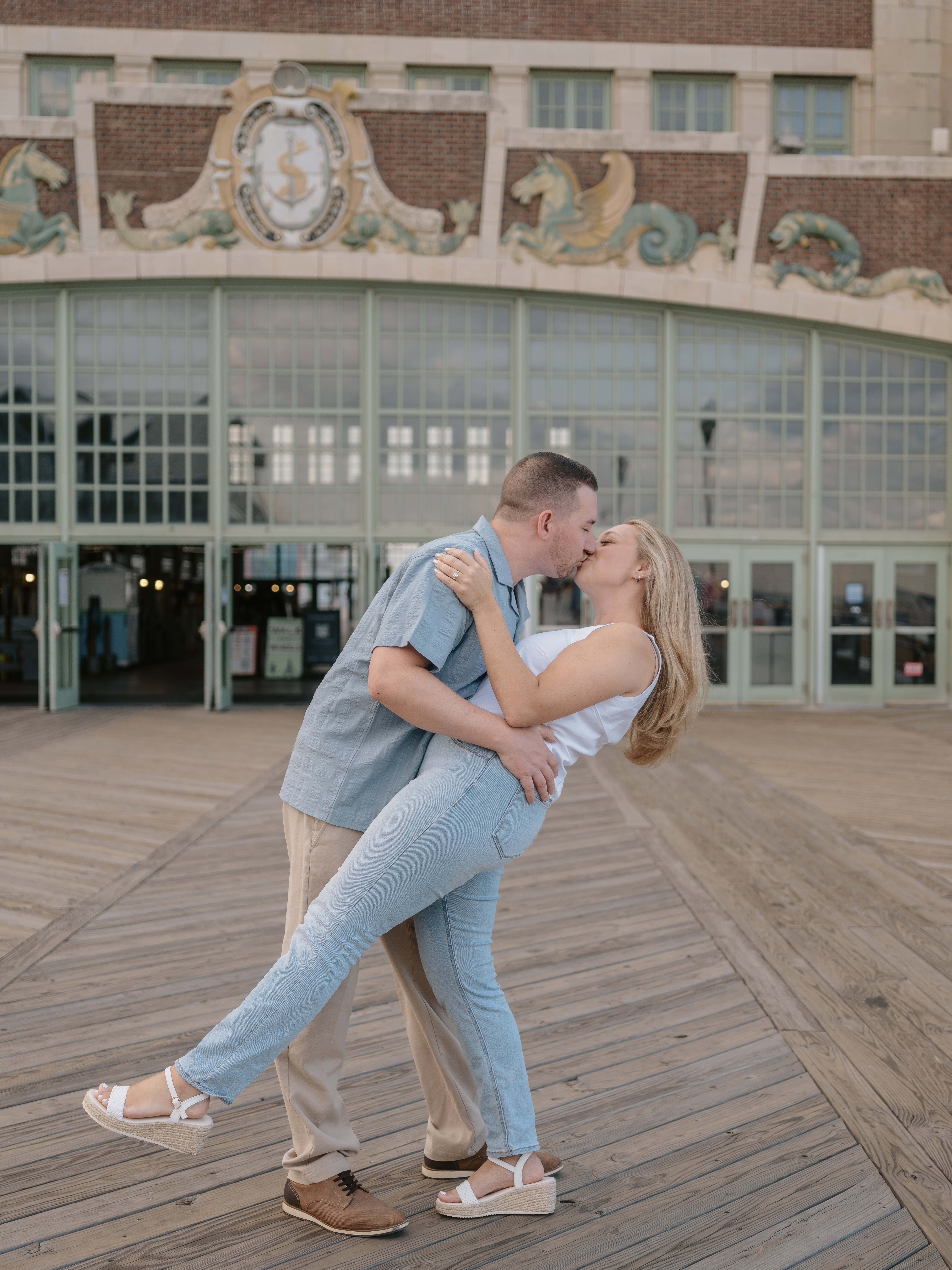 Groom dips bride and kiss on pier at Sunset for a Asbury Park Engagement Photo